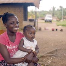 woman sits outside her house with her daughter on her lap