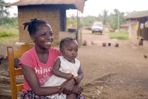 woman sits outside her house with her daughter on her lap