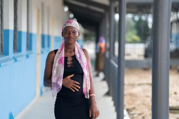 Pregnant woman holds her belly and smiles to the camera