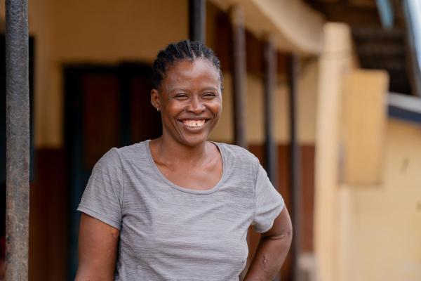 A smiling woman stands outdoors against the background of a building.