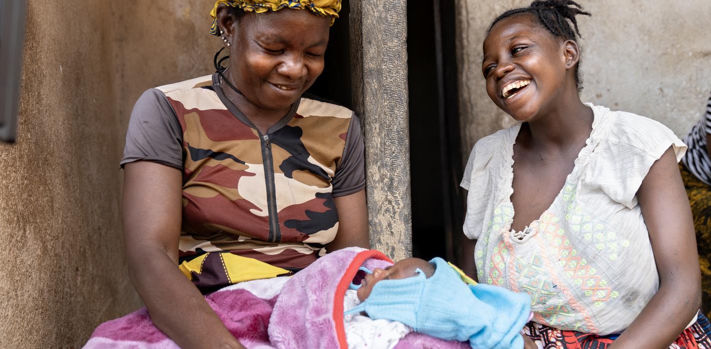woman is holding a baby on her lap, another woman is sitting next to her smiling