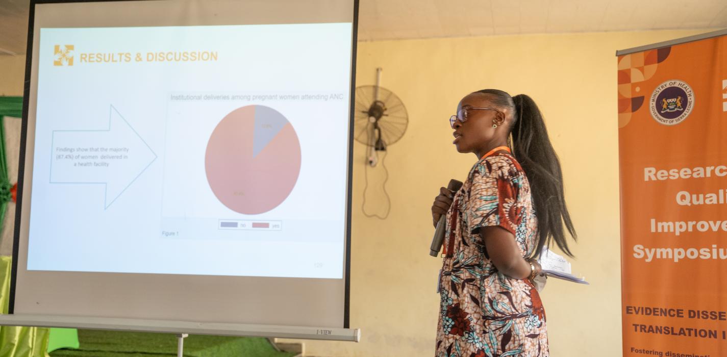 Woman standing in front of projector with data slide holding microphone