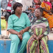 Midwife sits next to pregnant woman infront of house 