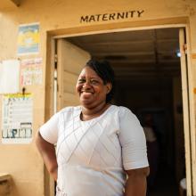 woman smiling at camera in front of door that reads maternity