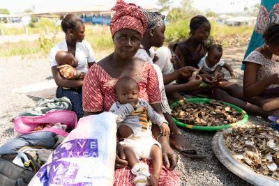 A woman sits under a tree with a baby in her lap