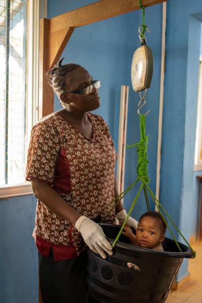 A nurse weighs a baby in a bucket weighing scale
