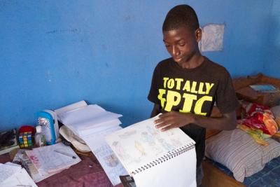 Mondeh stands in his bedroom and shows his artwork.