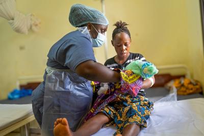 nurse is handing baby to mother who sits on hospital bed