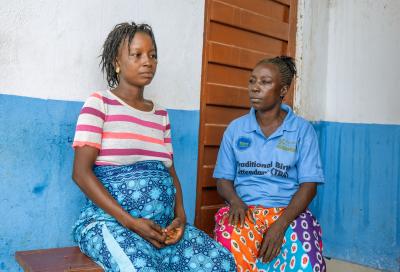 Pregnant woman sitting on bench with traditional birth attendant woman next to her