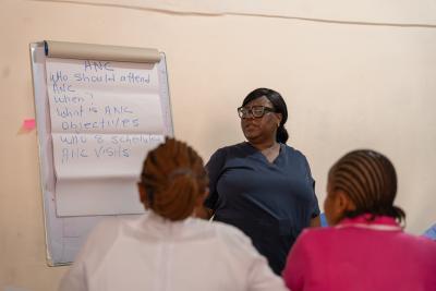 Woman stands next to flip chart teaching nurses sitting in a classroom
