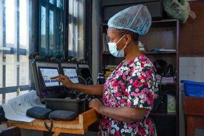 nurse in scrubs in front of a small computer inputting data