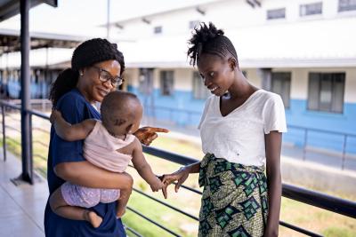 Midwive holds baby girl while mother stands next to them looking at her daughter