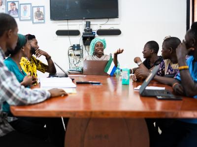 multiple people sit around a table with a woman in the center leading the meeting