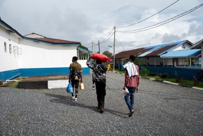 Two young men help Santigie M. Conteh (right), an MDR-TB patient, carry his food support package as he departs from Lakka Government Hospital.