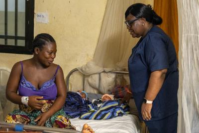 A clinician stands next to the bed of a new born baby and their mother
