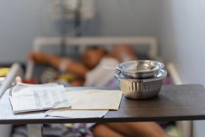 A metal bowl on a small table with documents, with a woman in the blurred background laying on a bed.