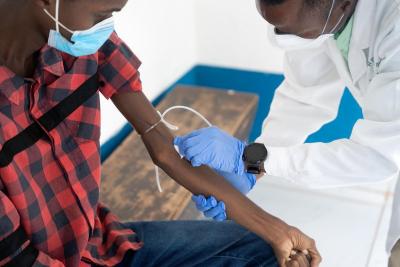 A laboratory technician draws blood from Santigie's left arm with a syringe.