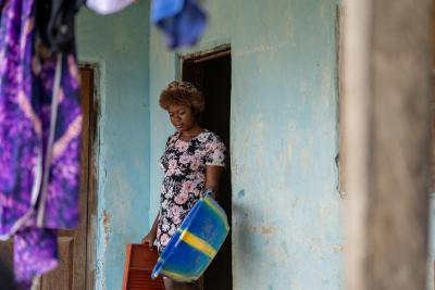 A woman in a wool hat carrying a basin and washboard through a door.